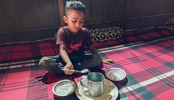 Young boy demonstrating how to prepare homemade oral rehydration salts with sugar, salt, and water