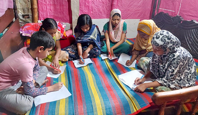 Group of children sitting on a mat writing essays during an educational competition