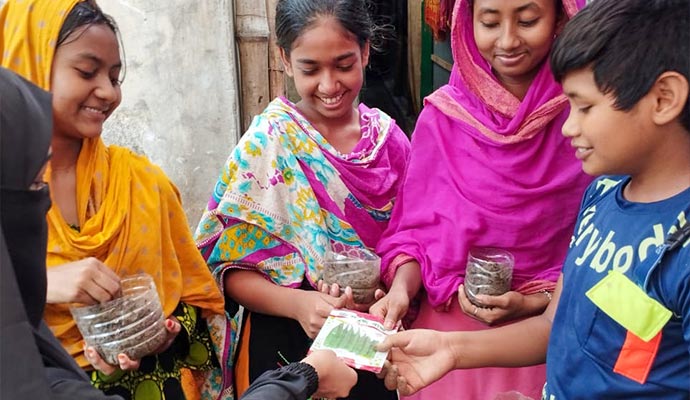 Smiling children holding recycled plastic bottle planters and a vegetable seed packet