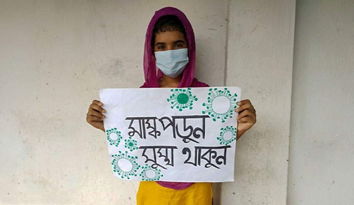 Young girl holding a handmade community health awareness poster with a protective mask